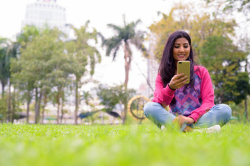 Happy young beautiful Persian woman using phone at the park