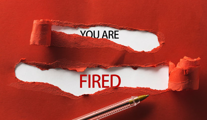 Red torn paper with inscription you are fired and pen close up