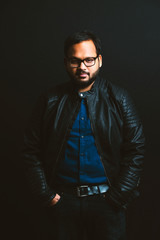 Fototapeta premium Close up of smiling Young Indian bearded man Wearing Eyeglasses, Looking at the Camera Against Black Wall Background