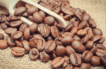 Heap of coffee grains with wooden scoop on jute burlap
