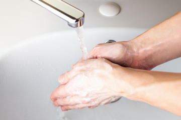 Fototapeta premium Washing hands with soap under running water in the bathroom over the sink. Hygiene concept for protection against coronavirus infection. Wet soapy hands. Banner background