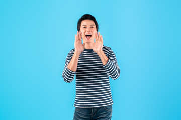 Young happy Asian man shout and announce with loud over blue background with copy space