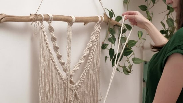 woman weaves macrame on a stick.
