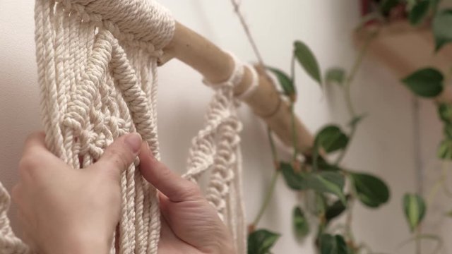 woman weaves macrame on a stick.