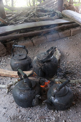 Old kettles with black soot on bonfire with woods