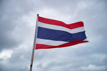 Waving Thai flag of Thailand with cloudy sky background.