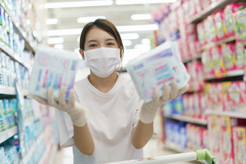 Woman wearing surgical mask and gloves,  buying sanitary napkin in supermarket. Panic shopping after coronavirus pandemic.
