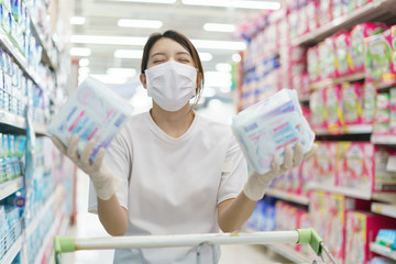 Woman wearing surgical mask and gloves,  buying sanitary napkin in supermarket. Panic shopping after coronavirus pandemic.