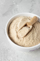 Buckwheat flour and a small wooden scoop with flour in a bowl, light grey concrete background. Gluten free flour, healthy nutrition. Top view.