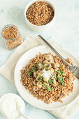 Buckwheat porridge with mushrooms and herbs in a ceramic plate on light grey concrete background. Vegan and vegetarian meal. Healthy content. Toned image. Top view. 