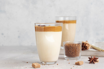 Iced Dalgona coffee in tall glass with spices. A trendy fluffy creamy whipped coffee. Korean coffee drink. Light grey concrete background. 