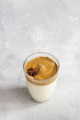 Iced Dalgona coffee in tall glass with spices. A trendy fluffy creamy whipped coffee. Korean coffee drink. Light grey concrete background. 