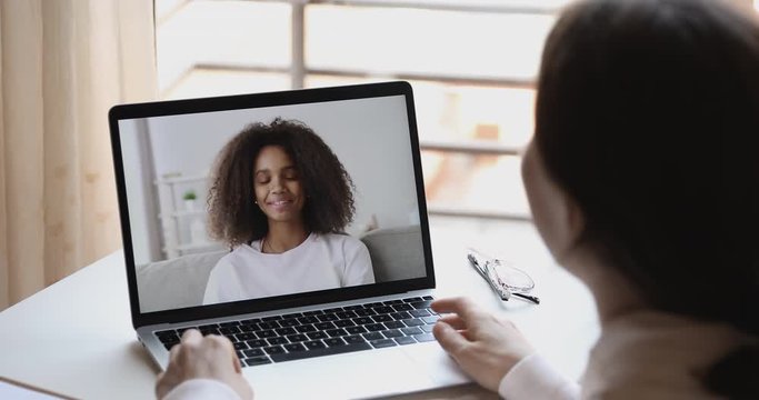 Over Shoulder View Of Caucasian Online Teacher, Remote Tutor Or Psychologist Conferencing With African School Girl Student On Distance Learning Video Call At Home. Online Study By Webcam Chat Concept