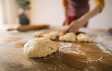 Selective focus of dough on kitchen table with cropped silhouete of woman wearing apron in background