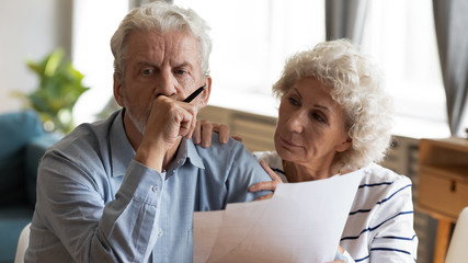Unhappy older couple reading documents, checking domestic bills, caring mature wife comforting sad...