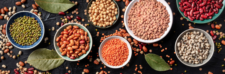 Legumes flat lay panorama, shot from the above on a black background. Lentils, soybeans, chickpeas,...