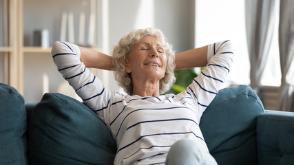 Smiling older woman leaning back, relaxing on cozy couch, happy mature senior female with hands...