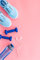 Fitness flat-lay with sneakers, dumbbells and headphones on pink table top view copy space