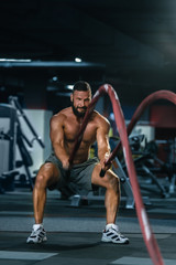 Fototapeta na wymiar Portrait of strong muscular man pulling heavy rope in gym