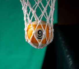 In billiard pocket a ball no. nine on a green backgound.