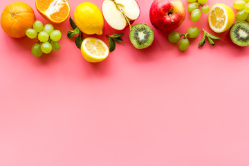 Fresh fruits background with citruses, apple, kiwi and grape on pink table top-down frame copy space