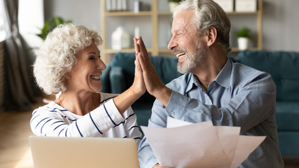 Excited older couple giving high five, mature family celebrating success, checking or paying domestic bills, planning budget, smiling mature man holding financial documents, reading good news - obrazy, fototapety, plakaty