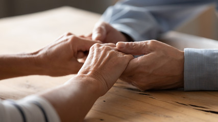 Close up older spouses holding hands on wooden table, loving caring mature man comforting senior...