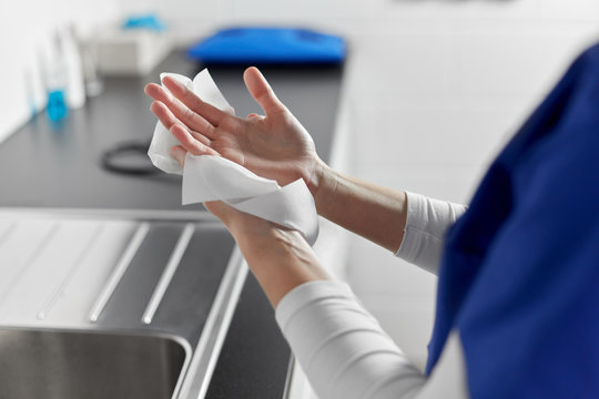 hygiene, health care and safety concept - close up of female doctor or nurse drying hands with paper tissue at hospital