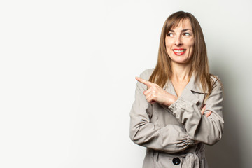 Portrait of a young friendly woman in a classic jacket points a finger to the side and smiles on an isolated light background. Emotional face. Gesture look at it, pay attention