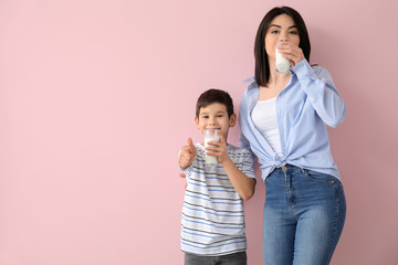 Mother with her little son drinking milk on color background