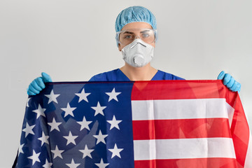 medicine, healthcare and pandemic concept - young female doctor or nurse wearing goggles and face protective mask or respirator for protection from virus disease holding flag of america