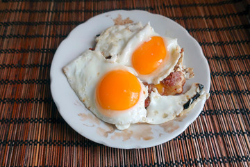 homemade breakfast of fried eggs from two eggs and a piece of fried meat on a plate