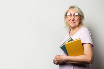 Portrait of an old friendly woman with smile in a casual t-shirt and glasses holds a stack of books on an isolated light background. Emotional face. Concept book club, leisure, education