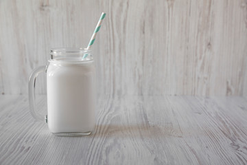 Coconut milk in a glass jar on a white wooden background, side view. Copy space.