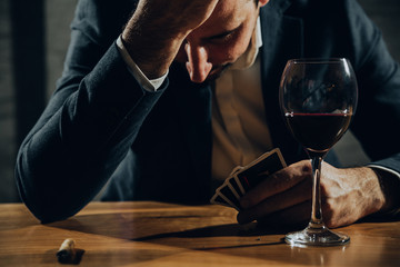 Close up of worried man playing card and drinking wine.	