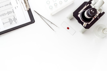 Fototapeta premium Microscope medical reserch. Hand holds blood sample. White table top-down copy space