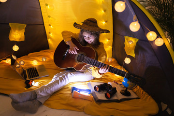 Little girl playing acoustic guitar under the tent in a living room.