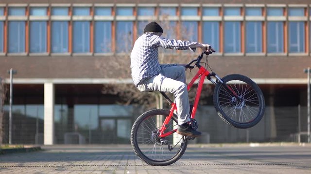 Cool young man wheelies with Mountainbike MTB Bike next urban building / Outdoor Action & Fun Sports