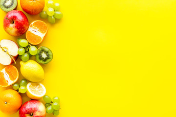 Oranges, lemon, apple, kiwi and grape - healthy food concept with fruits - on yellow background top-down frame copy space