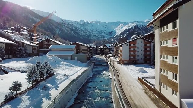 Aerial, drone shot over a river, in middle of buildings in the Zermatt village, sunny, winter day, in Valais, Switzerland