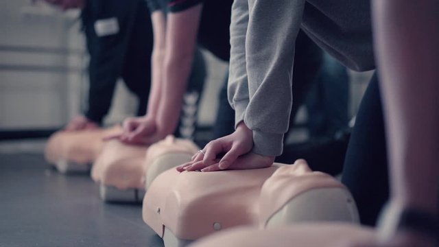 Group of hands, performing cpr on test dolls.