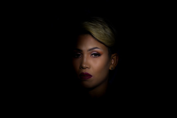 Portait photography of the face of a young asian woman with black background. Spot light portrait. Expressive girl portrait on dark background. Girl with a spot of light on her face. Sad face.