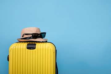 Closeup of yellow suitcase with hat and sunglasses on a blue background