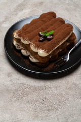 Classic tiramisu dessert on ceramic plate on light grey concrete background