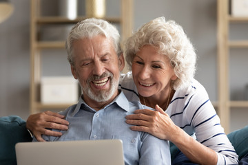 Smiling older couple looking at laptop screen together close up, mature woman and man making video...