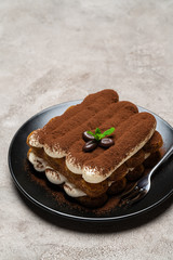Classic tiramisu dessert on ceramic plate on light grey concrete background