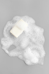 Soap bar with bubbles on grey background top-down