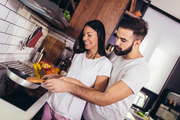 Woman preparing food at the stove with partner behind her in kitchen