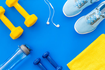 Sport flat-lay with dumbbells, towel, headphones on blue background top-down