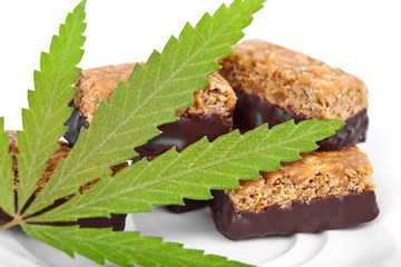 Candy with the addition of medical cannabis CBD for recreational use to relax body and mind. Sweet cannabis candy CBD Cannabidiol next to green leaves of marijuana on white isolated background